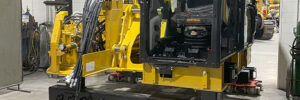 Large yellow construction equipment is being moved inside a warehouse using a flat, wheeled robotic platform.
